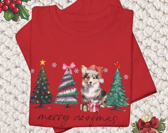 Op de afbeelding: Rood T-shirt met een kerstthema met een corgi-hond die een kerstmanmuts draagt en voor drie gedecoreerde kerstboom staat. De tekst "merry woofmas" staat onder de afbeelding.