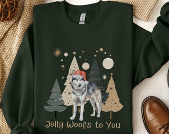Puede incluir: Una sudadera verde oscuro con un diseño navideño que presenta un lobo con un gorro de Papá Noel frente a árboles de Navidad estilizados. El texto "Jolly Woofs to You" está impreso debajo de la imagen.