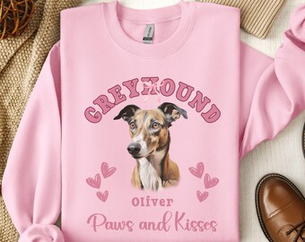 Könnte beinhalten: Rosafarbener Pullover mit einer Illustration eines Windhundes, dem Text "Greyhound", einem rosa Band, dem Namen "Oliver" und dem Spruch "Paws and Kisses".