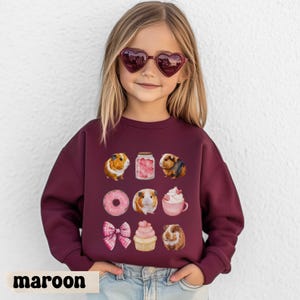 Könnte beinhalten: Burgunderfarbenes Sweatshirt mit Illustrationen von Meerschweinchen, einem Glas mit Herzen, einem Donut, einer Schleife, einem Cupcake und einer Tasse Schlagsahne. Das Wort "maroon" ist unten aufgedruckt.