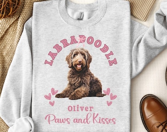 May include: A gray sweatshirt with a pink graphic of a brown Labradoodle dog. The graphic says "Labradoodle" in a pink arch with a pink heart above the word "Labradoodle". The graphic also includes the dog's name "Oliver" and the text "Paws and Kisses".