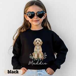 Può includere: Una felpa nera a maniche lunghe con la grafica di un cane marrone chiaro seduto tra fiori colorati. Sotto il cane, il nome Maddie è stampato in corsivo bianco. La felpa presenta un girocollo e maniche lunghe.