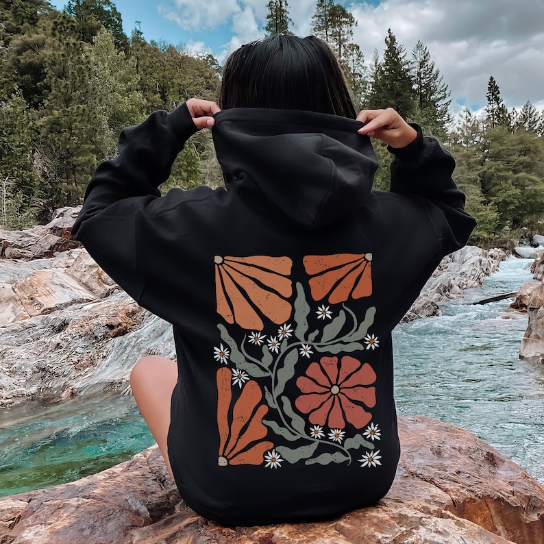 May include: Black hooded sweatshirt with a floral design on the back. The design features orange, red and green flowers with white accents.
