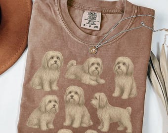 May include: Brown Comfort Colors t-shirt featuring multiple illustrations of a light brown dog breed. The shirt has a crew neck and the Comfort Colors brand tag is visible. A silver necklace with a pendant is draped across the shirt.
