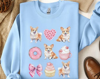 May include: Light blue sweatshirt with a pattern of pink hearts, donuts, cupcakes, and corgis. The corgis are wearing pink collars and have pink hearts on their chests.