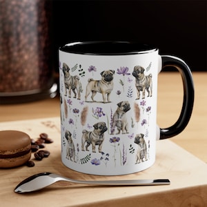 May include: White ceramic mug with a black rim and handle. The mug features a repeating pattern of pugs and flowers in shades of purple, pink, and brown.