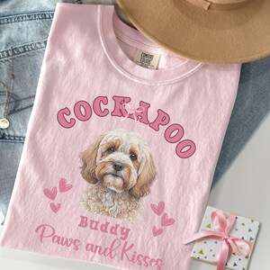 May include: Pink t-shirt featuring a Cockapoo dog illustration, the words "Cockapoo", "Buddy", "Paws and Kisses", and pink hearts.