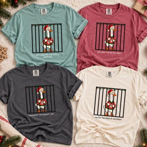 Peut inclure: Quatre t-shirts à manches courtes vert sauge, bordeaux, gris anthracite et crème. Chacun présente un graphique d'oie avec un bonnet de Noël et un pull derrière des barreaux avec le texte : Gift-wrapped the office supplies, Declined the office party, Laminated the naughty list, et Muted the boss by accident.