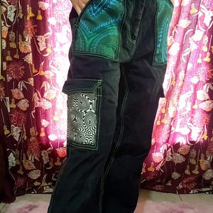 May include: Black cargo pants with white stitching and unique pocket designs. The front pockets feature a swirling green and blue pattern, while the side pockets showcase a black and white geometric design. A stylish and eye-catching garment.