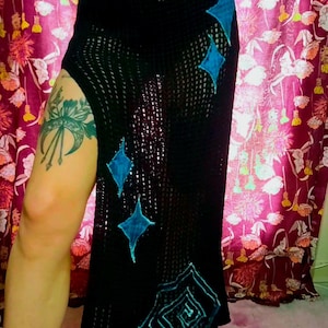 May include: Black crochet skirt with a high slit and turquoise diamond-shaped accents. The skirt has a fitted waistband and a flowing, open-weave design. The turquoise accents are hand-stitched onto the skirt.