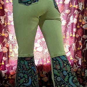 May include: Light green denim pants with flared bottoms and decorative pockets. The pockets and flares feature a dark fabric with a colorful floral and paisley design. The pants are a unique and stylish fashion item.