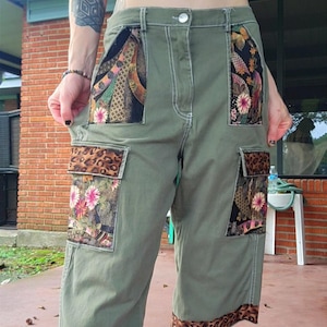 May include: Olive green cargo pants featuring contrasting fabric panels on the front pockets and thighs. The pockets are accented with floral patterns and leopard print trim, while the pant hems also feature a matching leopard print border.
