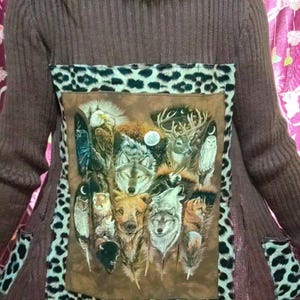 May include: Brown knit cardigan with a faux fur collar and leopard print accents. The back features a rectangular panel with a wildlife scene of wolves, owls, and deer. The pockets also have leopard print.