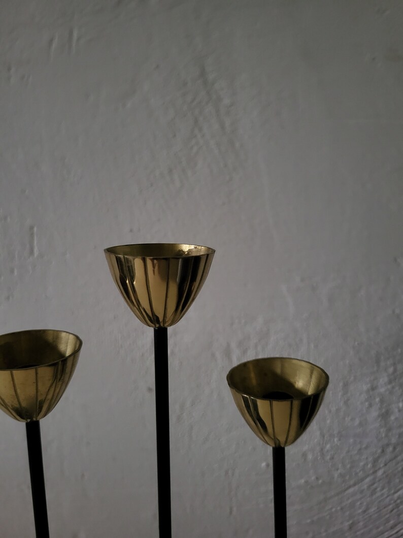 May include: A gold metal candle holder with three candle cups. The candle holder has a black metal base and three black metal stems.