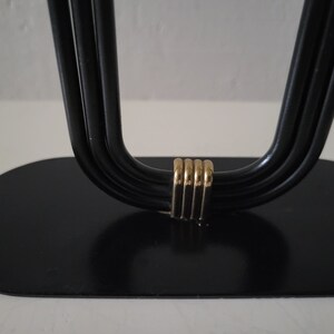 May include: Black metal candle holder with a gold accent. The holder has a rounded base and four arms that curve upwards.