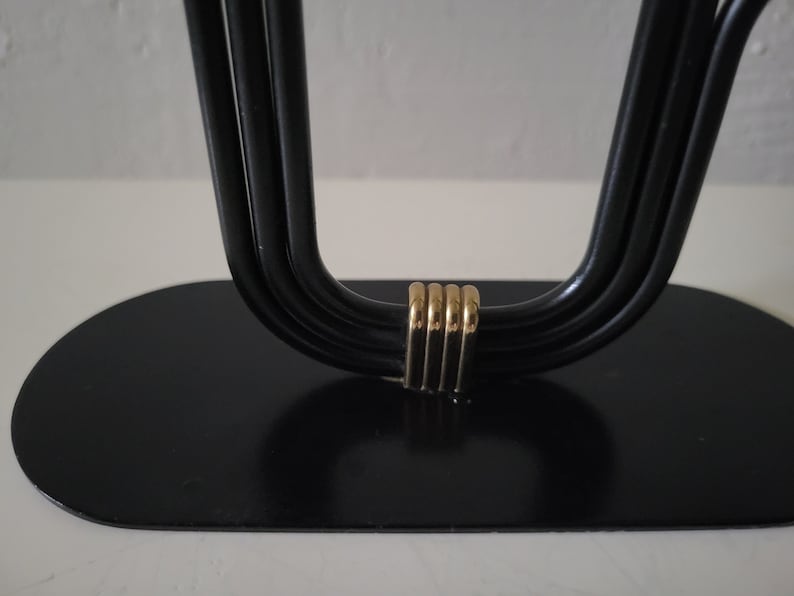 May include: Black metal candle holder with a gold accent. The holder has a rounded base and four arms that curve upwards.