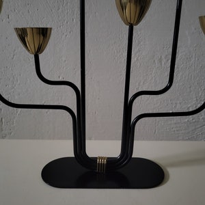 May include: A black metal candelabra with five gold candle holders. The candelabra has a curved design and a black base.