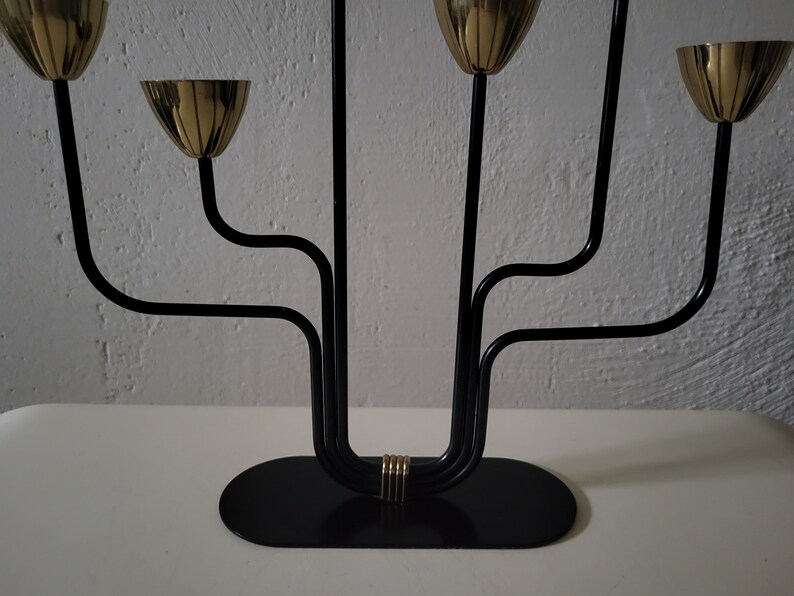 May include: A black metal candelabra with five gold candle holders. The candelabra has a curved design and a black base.