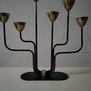 May include: A black metal candelabra with six gold candle holders. The candelabra has a curved design and a black base.