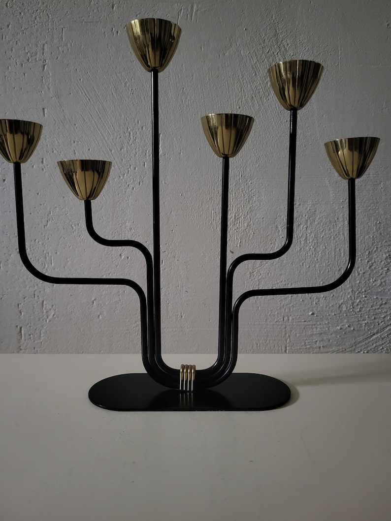 May include: A black metal candelabra with six gold candle holders. The candelabra has a curved design and a black base.