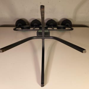 May include: Black metal candle holder with five candle cups. The holder has a unique design with a central vertical support and three legs that extend outward.