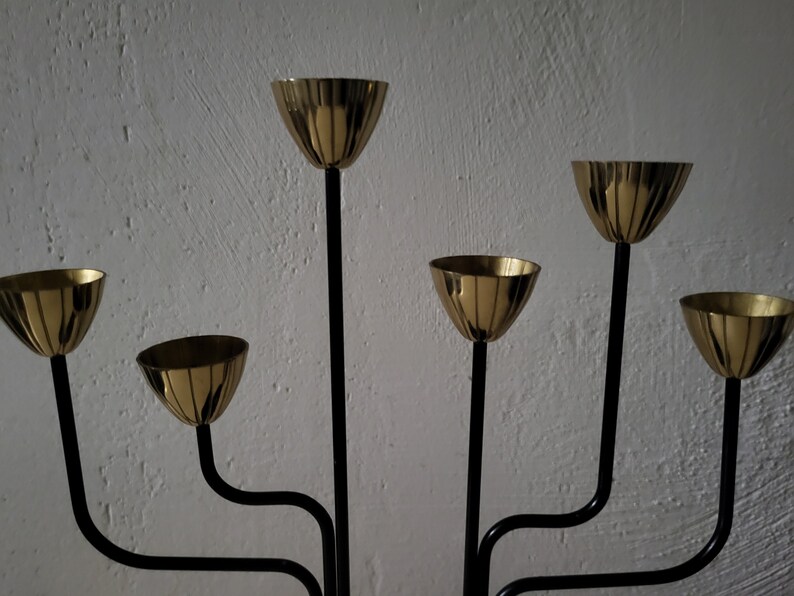 May include: A black metal candelabra with six gold candle holders. The candelabra has a modern design with curved arms.