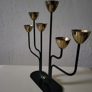 May include: A black metal candelabra with five gold candle holders. The candelabra has a modern design with curved arms and a circular base.
