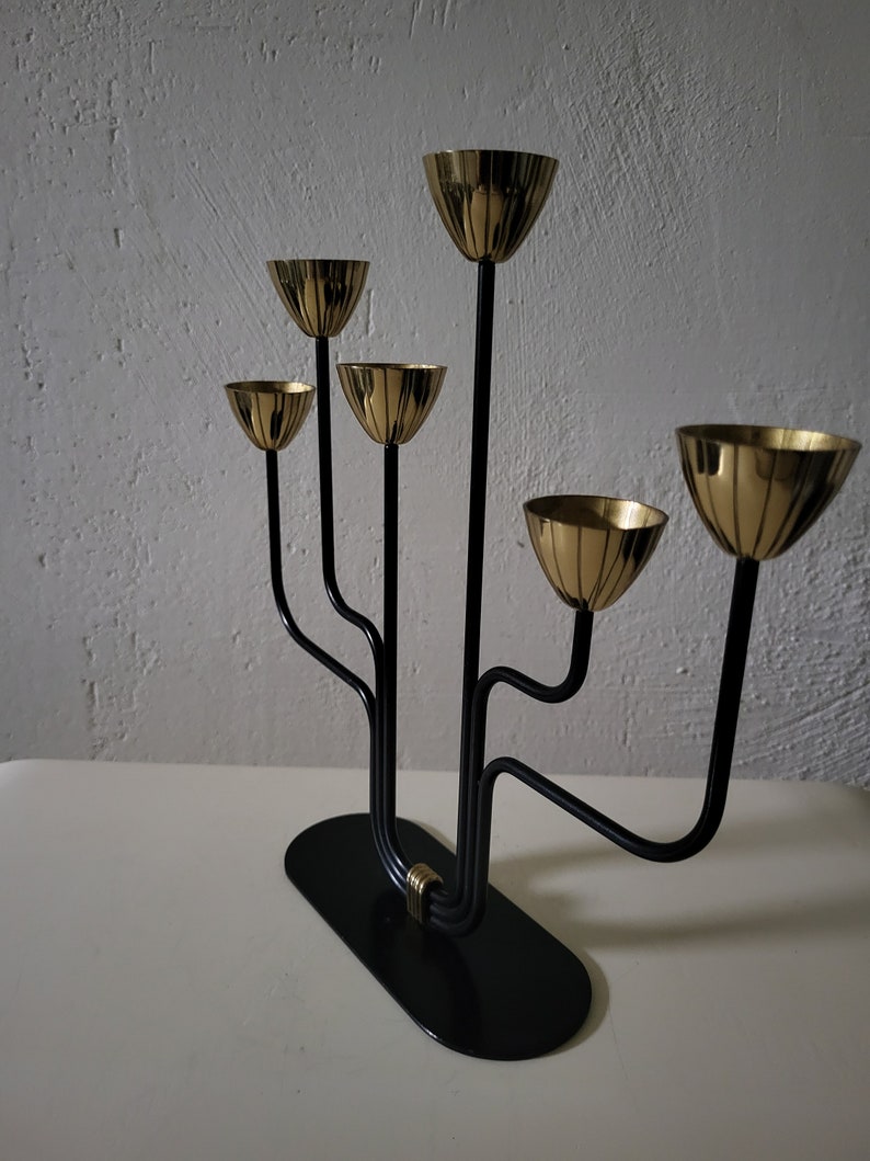 May include: A black metal candelabra with five gold candle holders. The candelabra has a modern design with curved arms and a circular base.