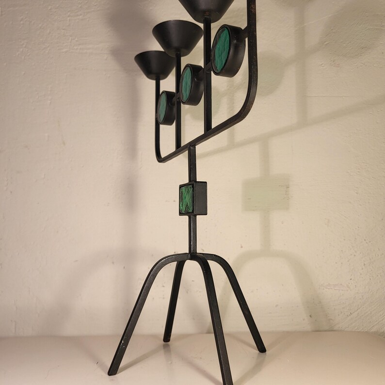 May include: A black metal candelabra with four candle holders and a green stone design. The candelabra has a tripod base.