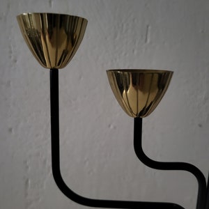 May include: A black metal candle holder with three gold-toned candle cups. The candle holder has a modern design with curved lines.
