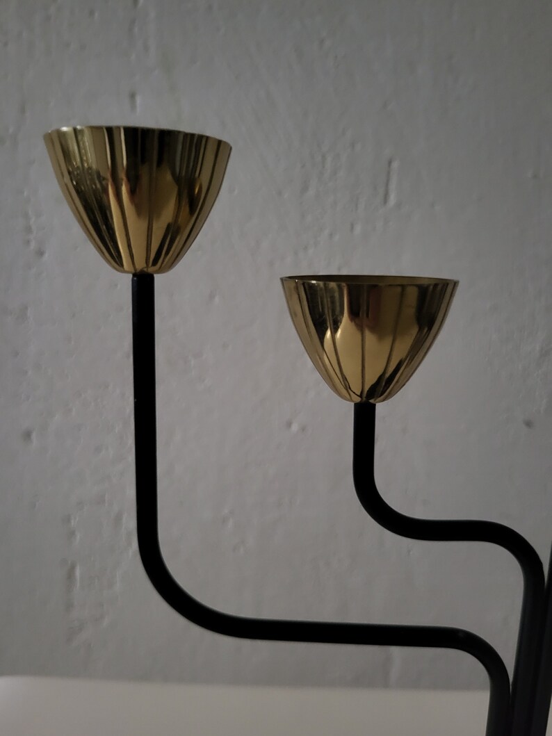 May include: A black metal candle holder with three gold-toned candle cups. The candle holder has a modern design with curved lines.
