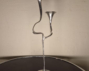 May include: A silver-toned metal candelabra featuring two candle holders at different heights. The structure consists of a single base that branches into two slender, curved stems, each topped with a flared, funnel-shaped cup for candles.