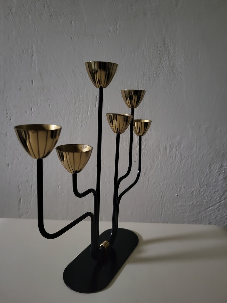 May include: A black metal candelabra with five gold candle holders. The candelabra has a modern design with curved arms.