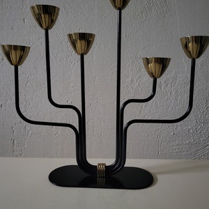 May include: A black metal candelabra with five gold candle holders. The candelabra has a curved design and a black base.