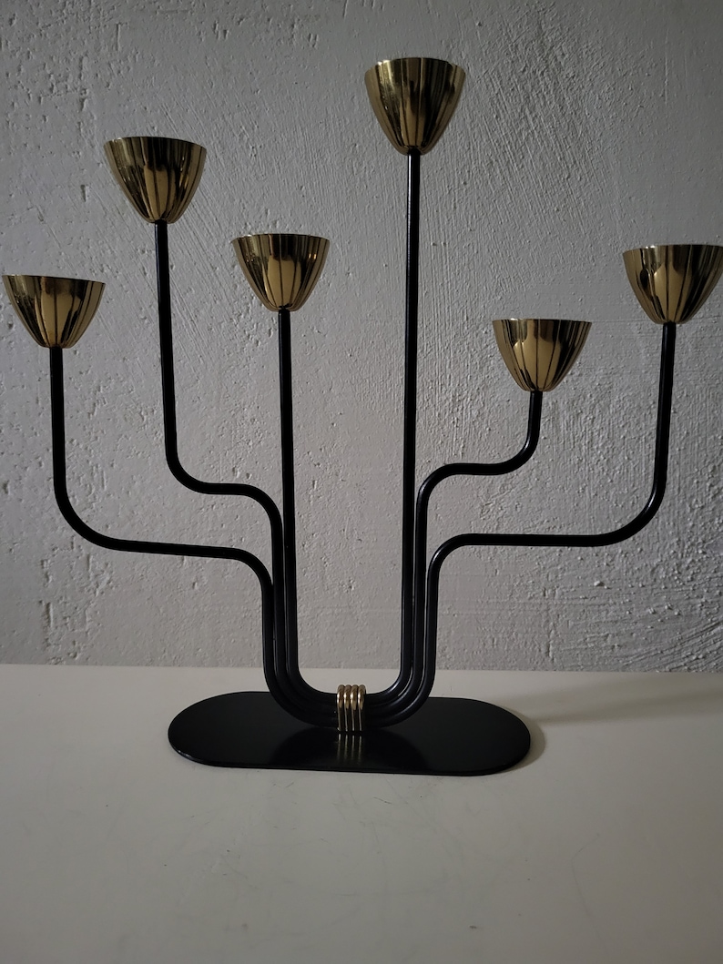May include: A black metal candelabra with five gold candle holders. The candelabra has a curved design and a black base.
