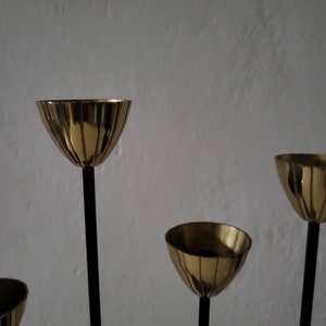 May include: A gold candle holder with five candle cups and black metal stems. The candle holder is on a white background.