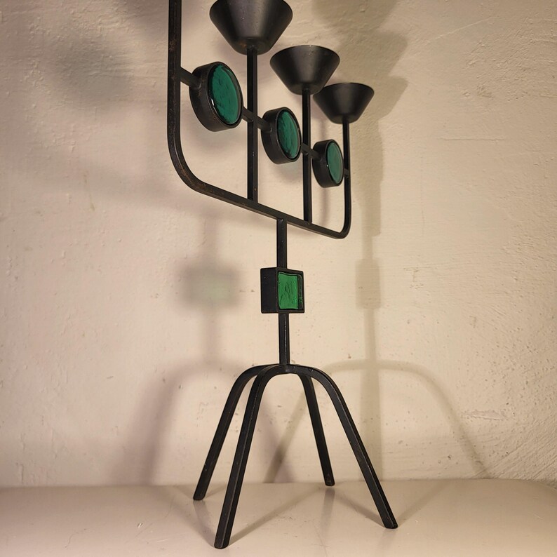 May include: A black metal candelabra with a tripod base and four candle holders. Each candle holder has a green glass accent.