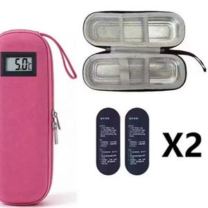 May include: A pink, elongated, zippered carrying case with a digital display showing 5.0°C. The case is shown closed with a wrist strap, and open to reveal a silver, insulated interior. Two dark blue, oval-shaped cooling packs are included.