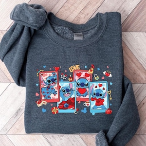 May include: A dark gray sweatshirt with a graphic print of Stitch from Lilo & Stitch. The graphic features Stitch in different poses with hearts and the word "LOVE".