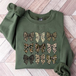 May include: A green sweatshirt with a pattern of nine camouflage bows on the front.