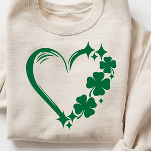 May include: A beige sweatshirt with a green shamrock heart design. The heart is outlined in green and filled with shamrocks.