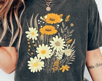 Könnte beinhalten: Ein dunkelgraues T-Shirt mit einem Vintage-Blumendruck mit gelben und weißen Gänseblümchen. Das Shirt hat einen Rundhalsausschnitt und kurze Ärmel.