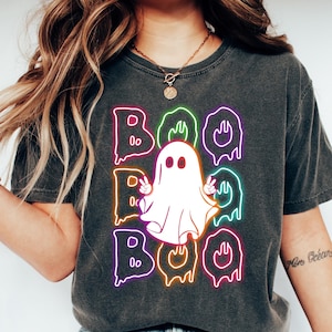 Puede incluir: Una camiseta gris oscuro con un gr&aacute;fico de ne&oacute;n de un fantasma con la palabra "BOO" escrita en letras de ne&oacute;n que gotean.