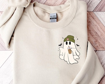 May include: A beige sweatshirt with a graphic of a ghost wearing a green beanie and holding a cup of coffee. The ghost is surrounded by bats and stars.