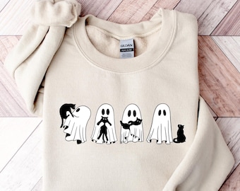 May include: A cream-coloured sweatshirt with a black and white graphic of four ghosts with cats. The ghosts have simple, round eyes and are draped in white sheets. One ghost has a cat on its head, another has a cat in its arms, and another has a cat with a mustache.