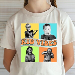 May include: A white t-shirt with a colorful graphic of four kids. The graphic has a yellow background with orange, blue, and green squares. The text "KID VIBES" is in a yellow, orange, and blue font.