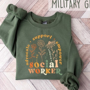 May include: A military green sweatshirt with a floral design and the text "support * advocate * empower * social worker" in a rainbow color scheme.