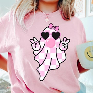 Peut inclure: T-shirt rose avec un fant&ocirc;me &agrave; carreaux rose et blanc portant des lunettes de soleil et un n&oelig;ud rose. Le fant&ocirc;me souffle une bulle.