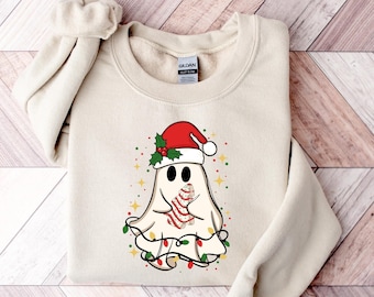 May include: A beige sweatshirt featuring a cartoon ghost wearing a Santa hat and holding a candy cane. The ghost is decorated with Christmas lights and holly. The design includes yellow stars and red, green, and white accents.