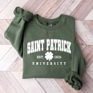 Puede incluir: Una sudadera verde con texto blanco que dice "Saint Patrick University" con un tr&eacute;bol y "Est. 1631" debajo.